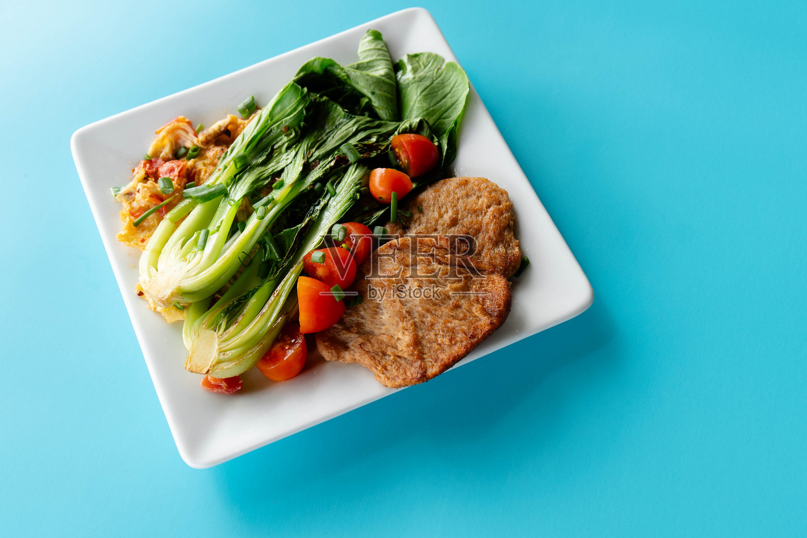 青菜沙拉配素肉和新鲜番茄，摆放在蓝色背景的方形盘子上照片摄影图片