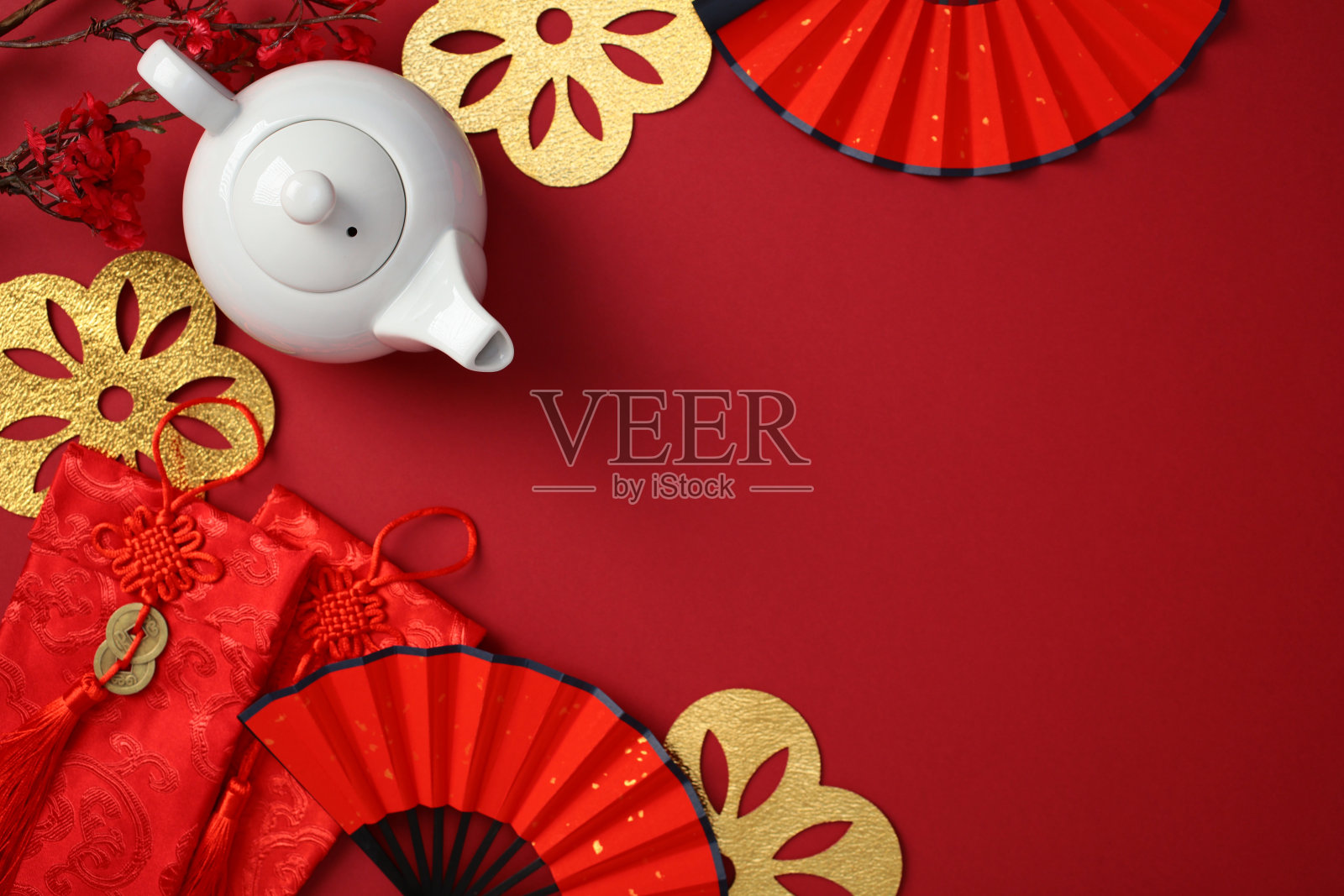 中国新年庆祝背景，白色茶壶、红色扇子、金色装饰和红包放在红色表面上照片摄影图片