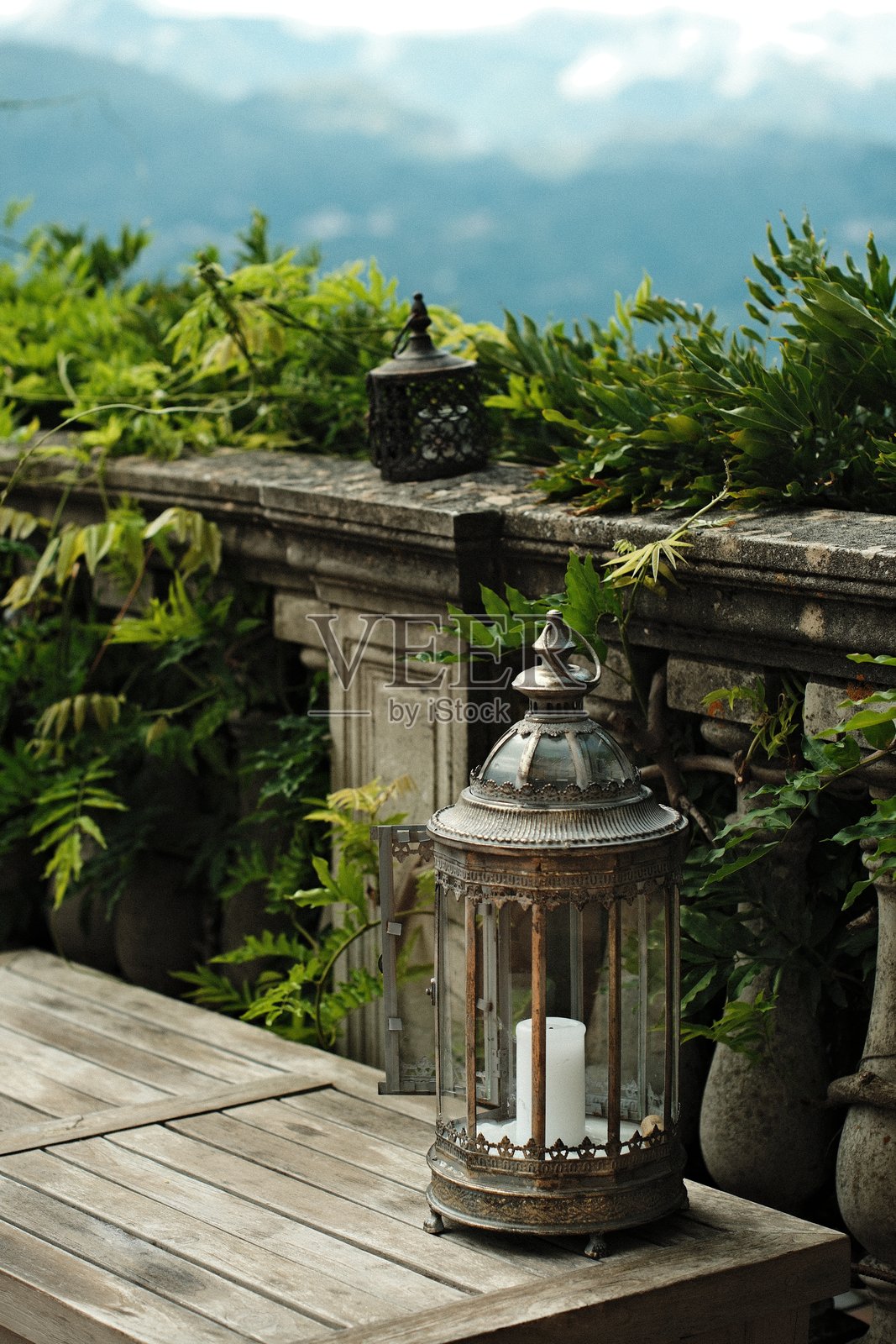 古老的灯笼放在木桌上，周围环绕着绿色植物，背景是宁静的山景。照片摄影图片