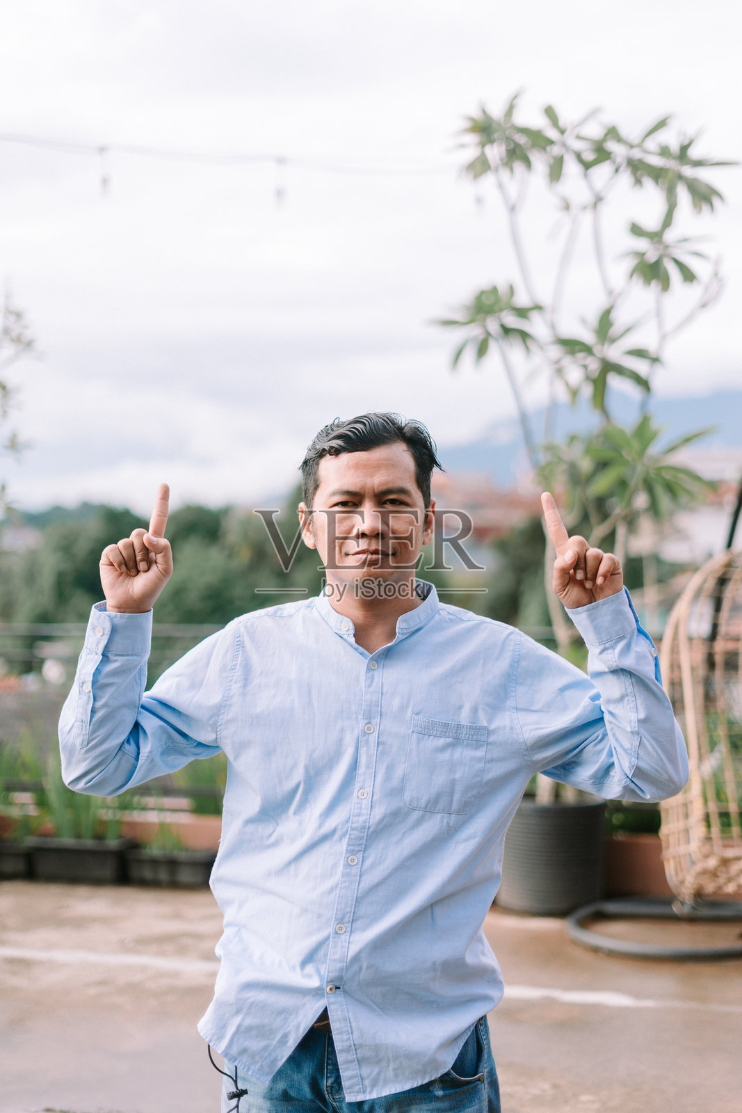 一位东南亚男子用一根手指指向上方，传达方向、专注或强调。照片摄影图片