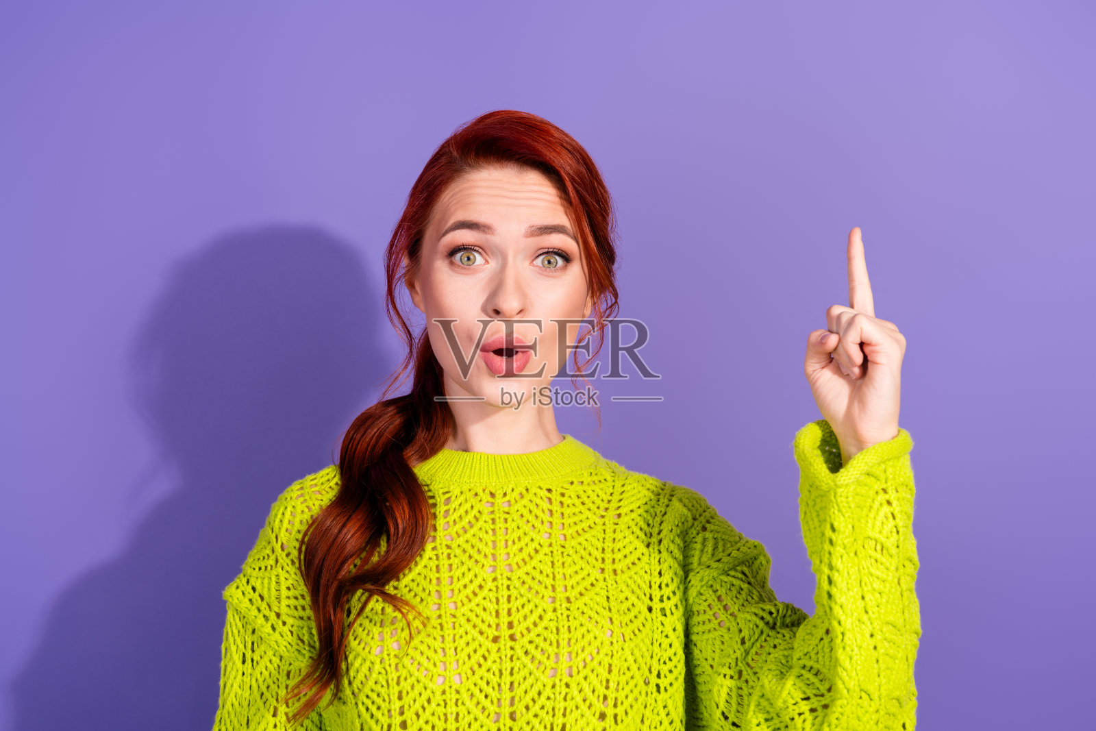 惊讶的年轻女性穿着绿色毛衣，指向充满活力的紫色背景，展现创意表达和想法。照片摄影图片