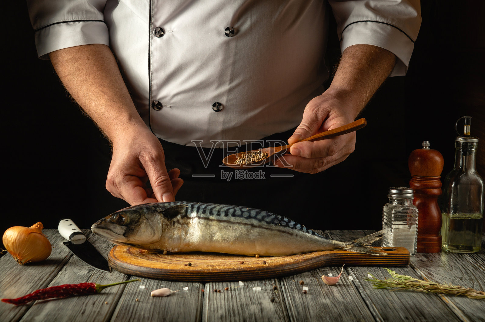 双手熟练地在木板上准备新鲜的鲭鱼，撒上香料。旁边有香气扑鼻的洋葱和油，营造出温馨厨房中的愉悦氛围。照片摄影图片