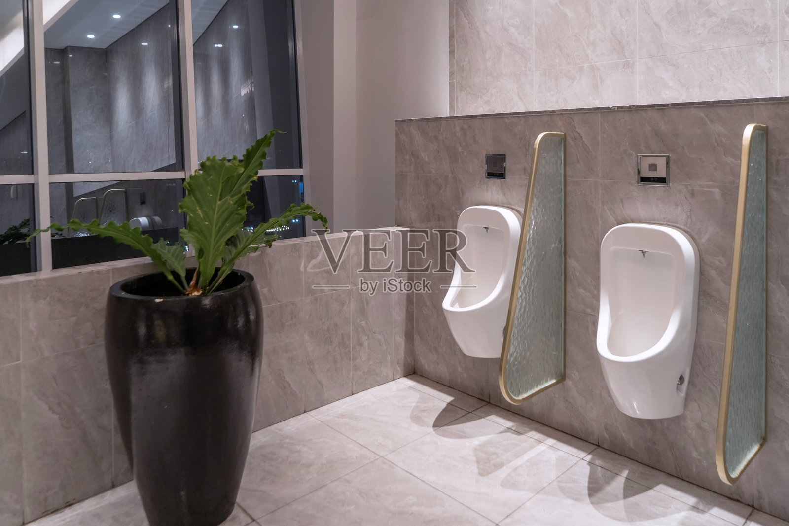 现代白色小便池在公共卫生间中排成一排，之间有隔板。旁边有一扇大窗户。照片摄影图片