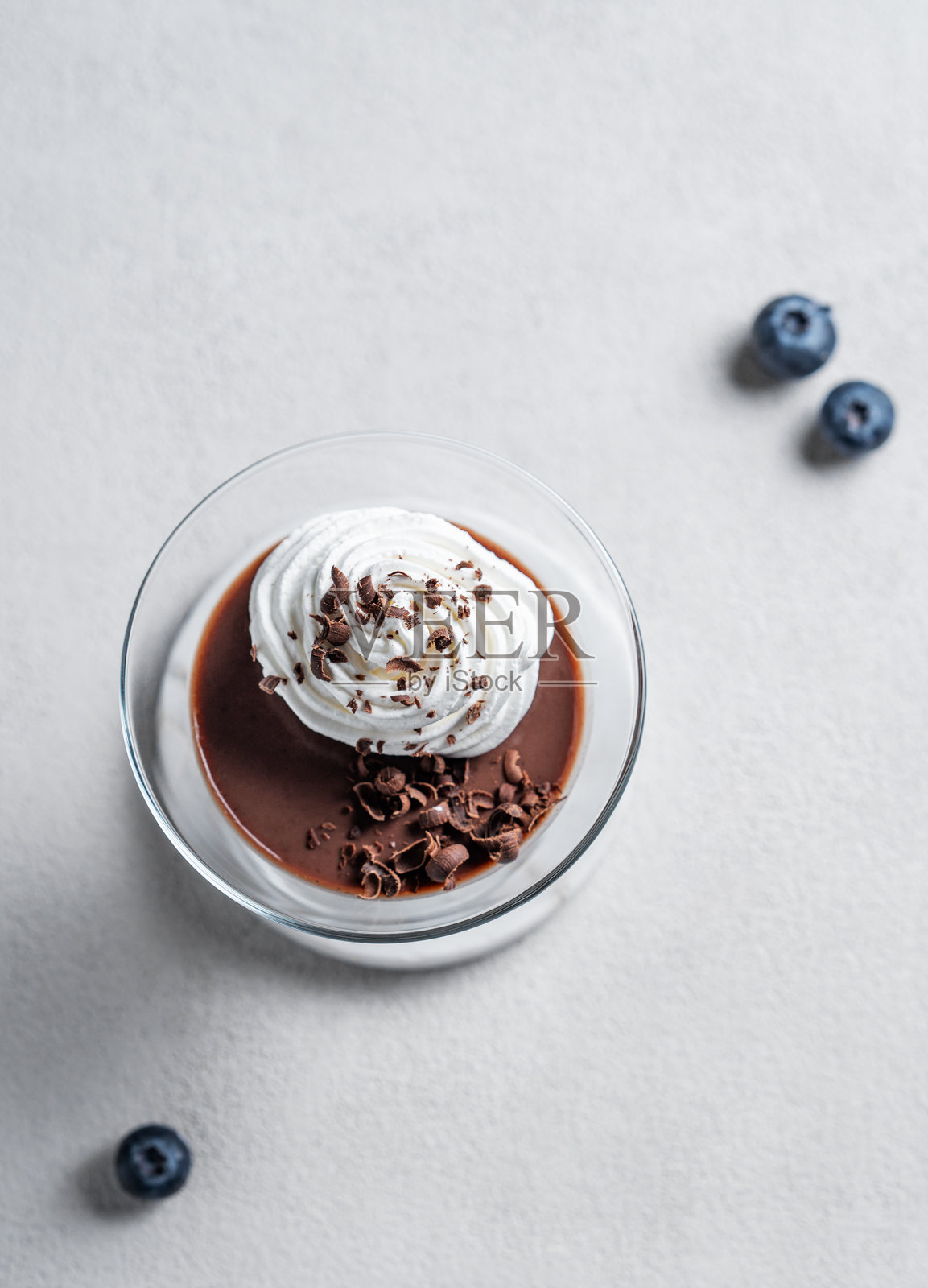 玻璃杯中的巧克力布丁，上面放有鲜奶油，背景为浅色，搭配浆果。照片摄影图片