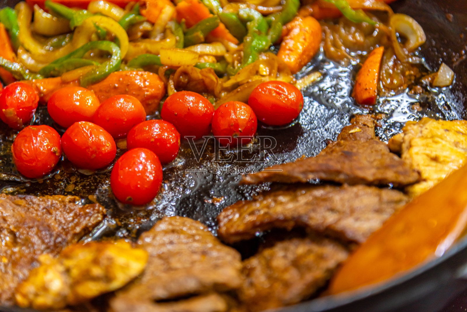 在煤气炉上用煎锅准备的牛排，配有洋葱、西红柿和辣椒。照片摄影图片