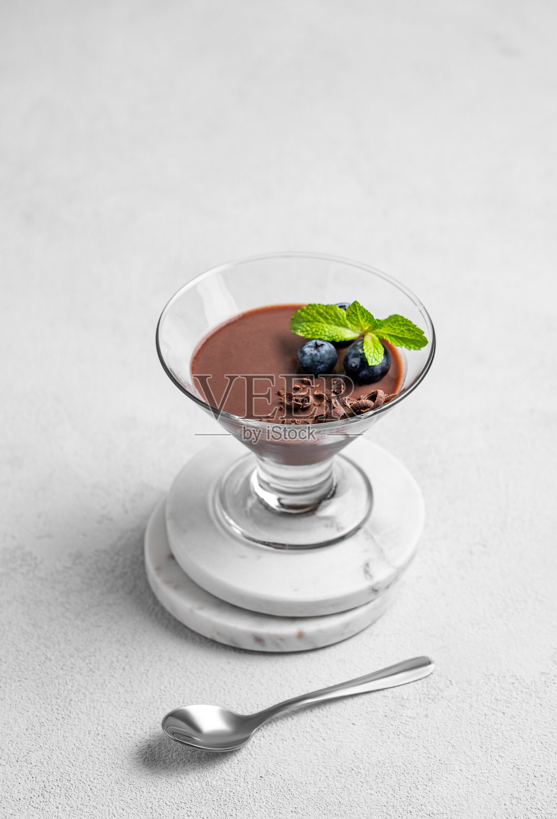 玻璃杯中的巧克力布丁，上面点缀着新鲜蓝莓和薄荷，背景为浅色。照片摄影图片