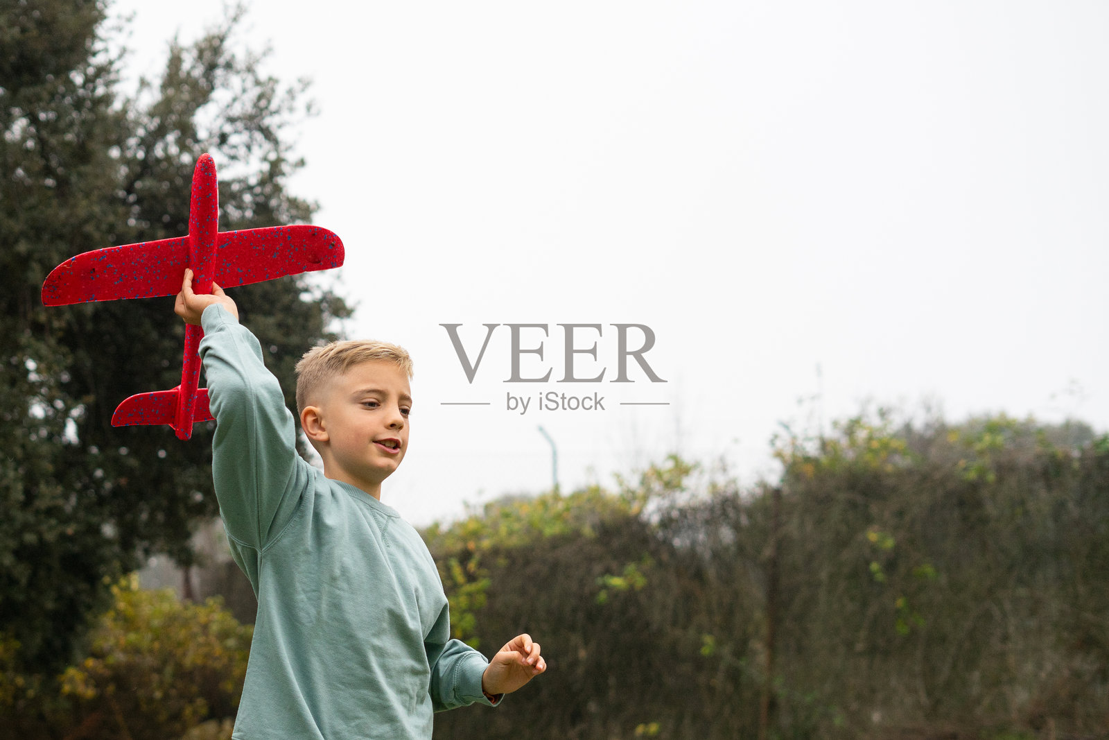 小男孩在花园里玩红色玩具飞机，梦想着飞翔照片摄影图片