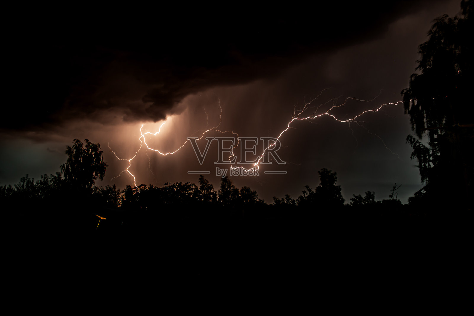 夜间森林中美丽的闪电在雷暴中引发了火灾，背景是阴暗的天空和雨水。照片摄影图片