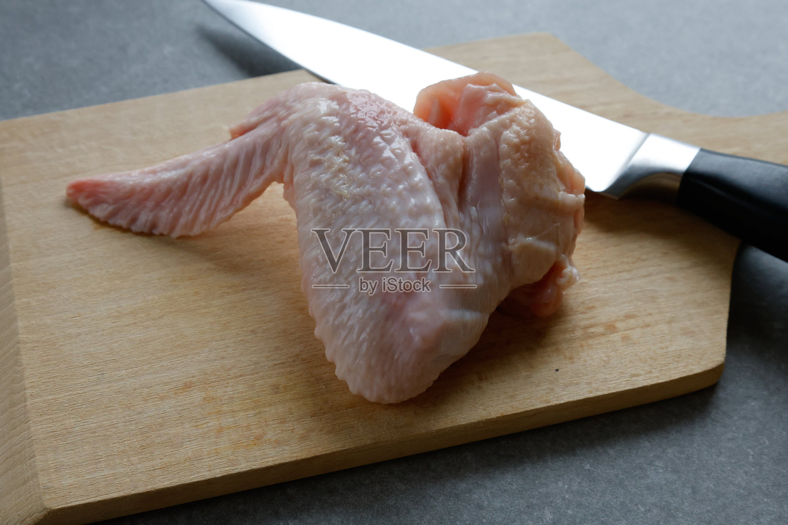 木砧板上的生鸡翅和一把刀。照片摄影图片