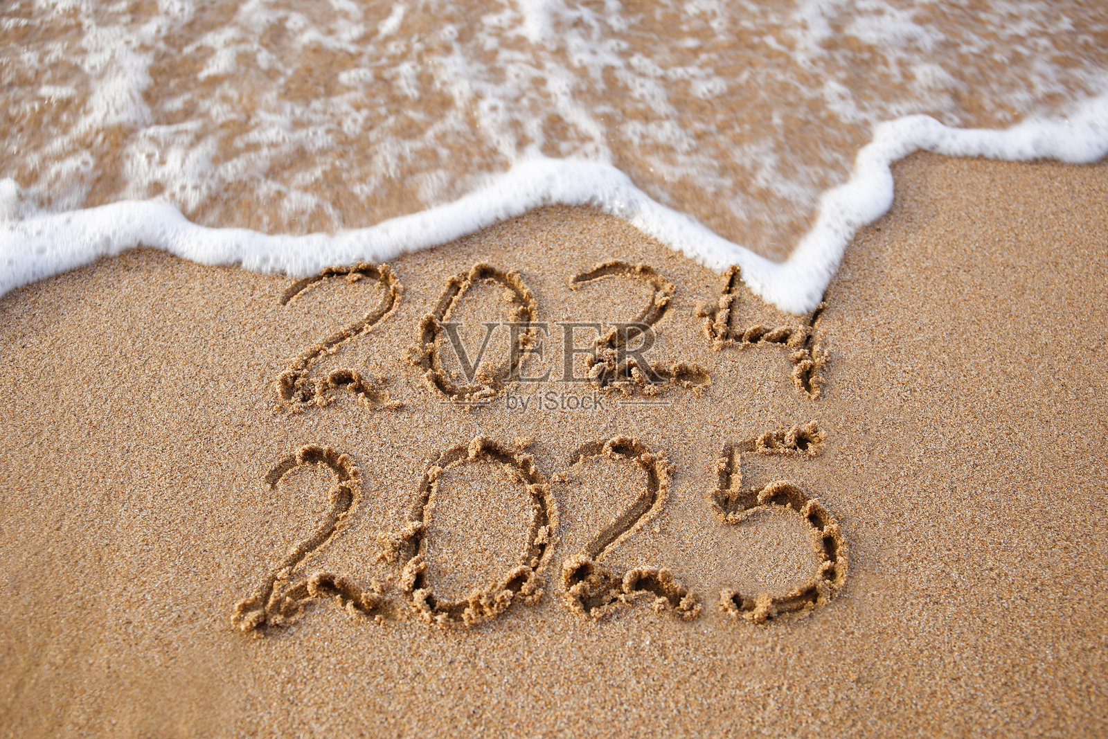 2024年和2025年写在沙滩上。海浪冲走了2024。新年快乐！照片摄影图片
