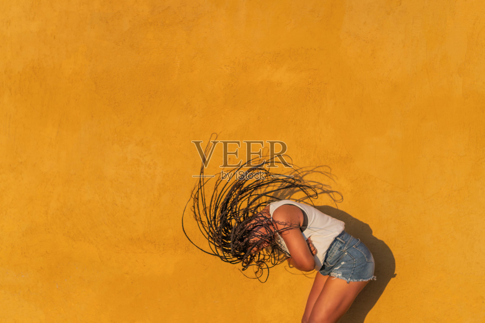 年轻女子在黄色墙壁前跳舞，长辫子随舞动而飘扬照片摄影图片