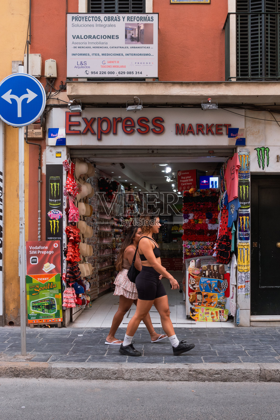 两个穿着夏季运动服的女孩在纪念品商店前的街道上走。照片摄影图片