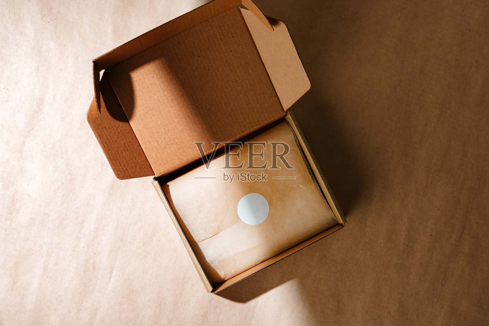 一个密封的牛皮纸盒，里面装着一个包裹的物品，放置在一个有纹理的棕色表面上，营造出开箱体验。照片摄影图片