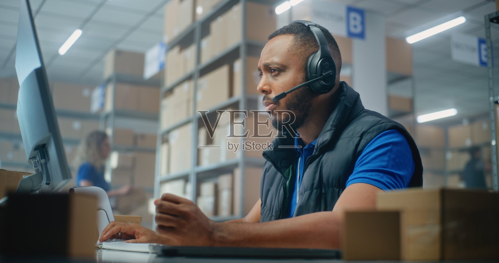 非裔美国人物流客户支持专员佩戴耳机与客户交谈，使用电脑照片摄影图片