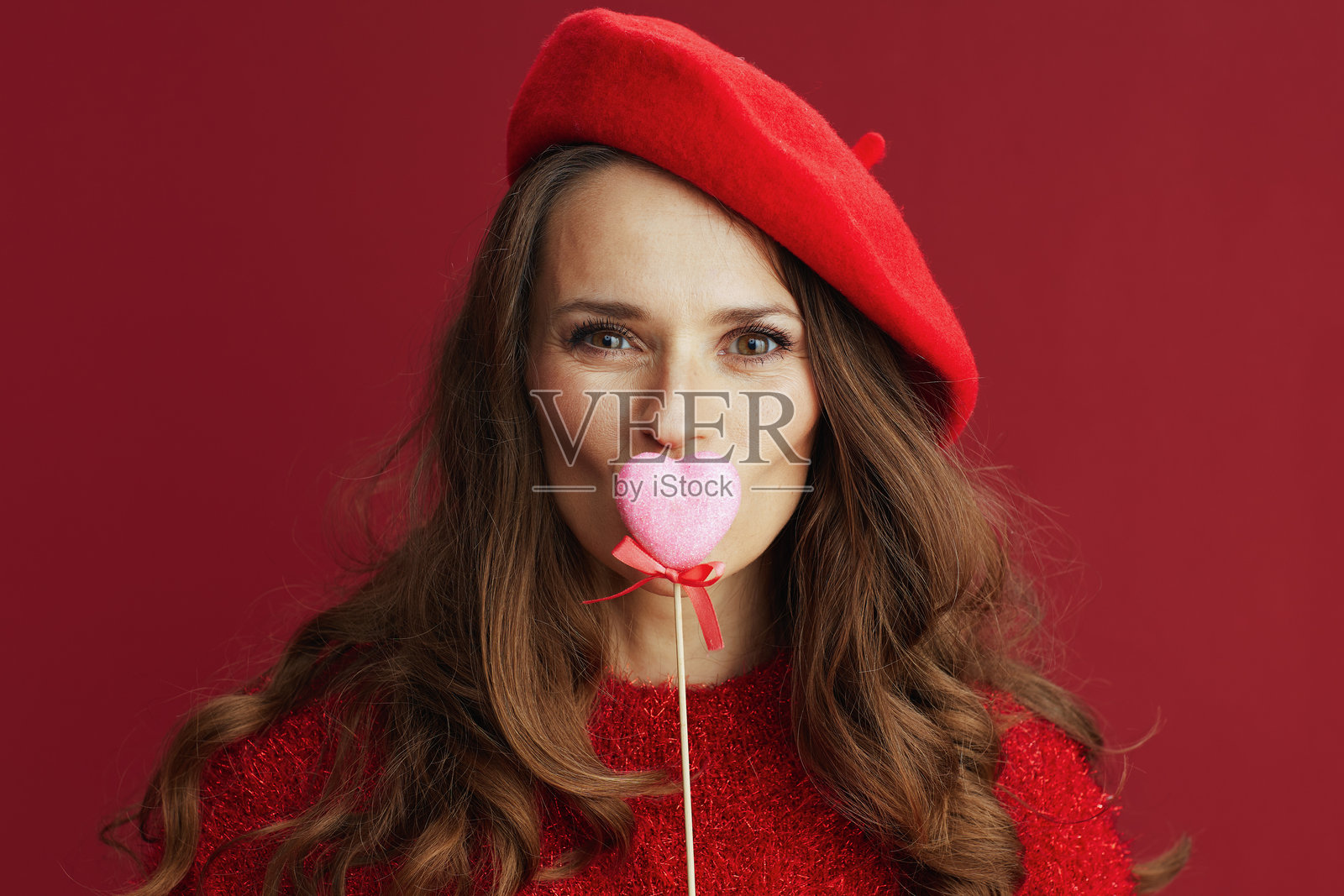 优雅的女性穿着红色毛衣和贝雷帽，手持心形棒子照片摄影图片