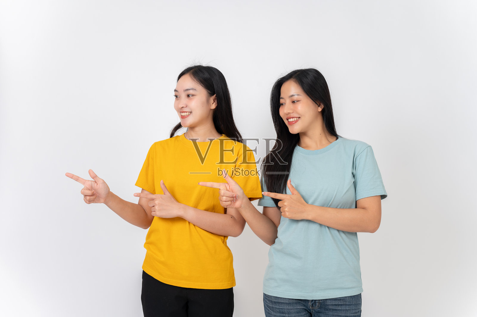 两个年轻、快乐的亚洲女性朋友用手指指向空旷的地方。照片摄影图片