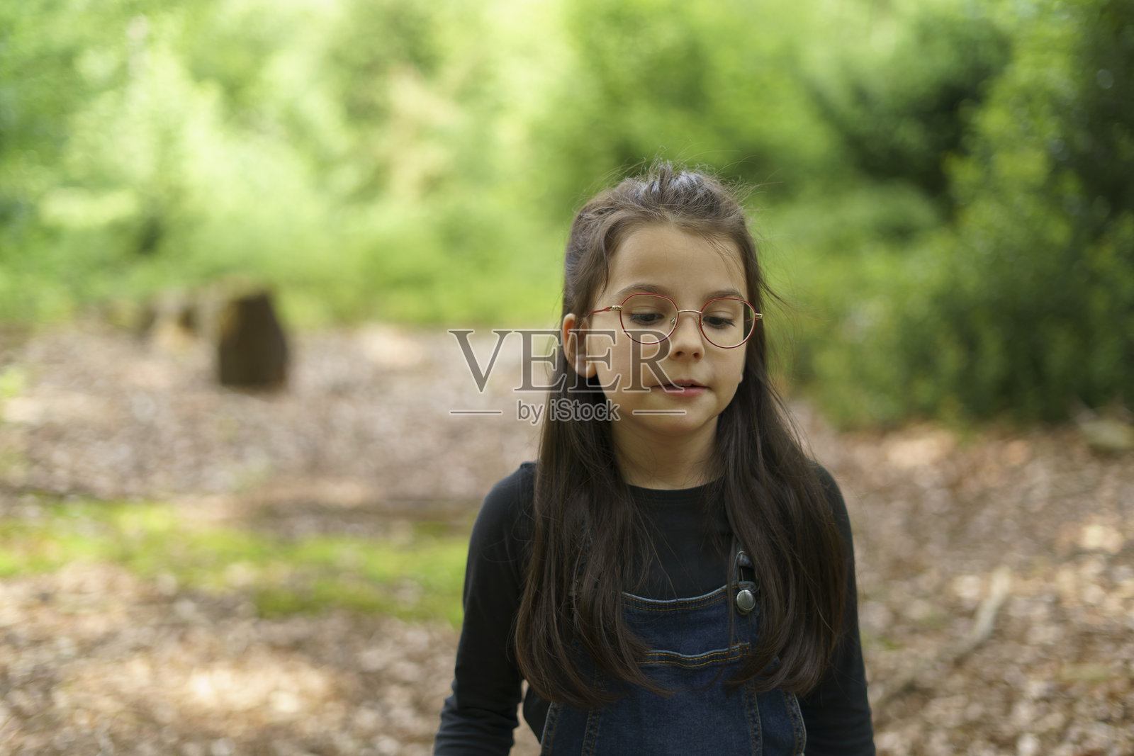 夏天在森林里，穿着牛仔工装和眼镜的小女孩。儿童乐趣和户外游戏的概念。照片摄影图片