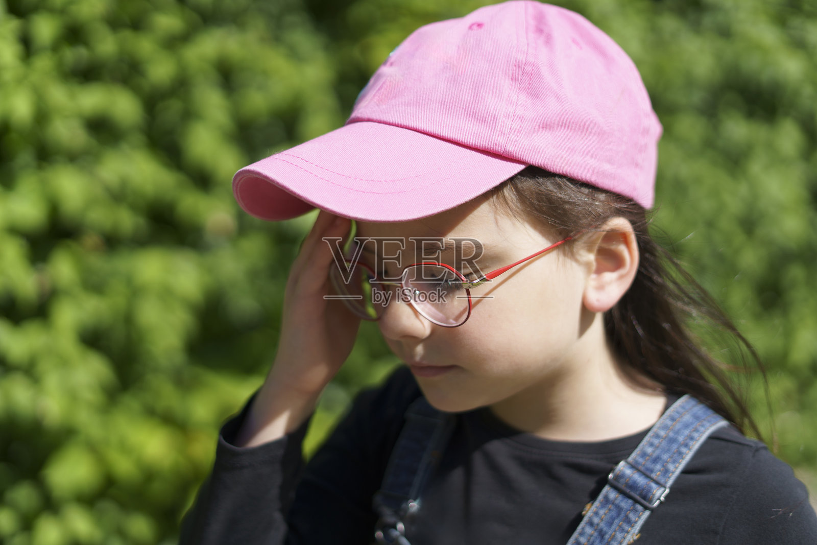 夏季户外，戴着粉色棒球帽和眼镜的小女孩显得格外开心。儿童旅行、乐趣与健康的概念。照片摄影图片