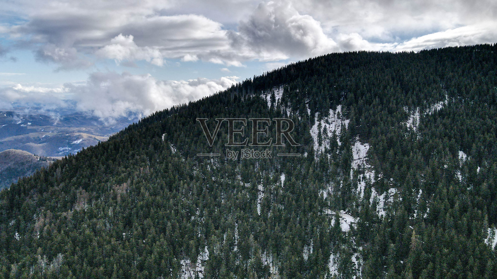 雪覆盖的山脉俯瞰图，正在缓慢融化，远处阳光照耀的山峰在充满云彩的蔚蓝天空下，展现出宁静的阿尔卑斯风光。照片摄影图片