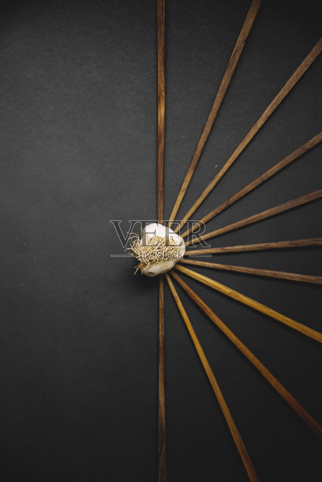 一个独特的蒜头，创意地展示在黑色背景上，周围有放射状的木棍，突显了极简主义和艺术化的食品造型，象征着乡村烹饪主题。照片摄影图片