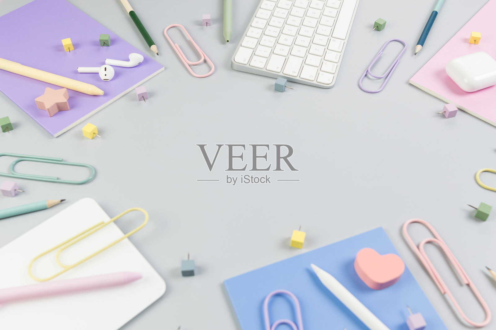 灰色背景上的白色键盘、鼠标、触控板、耳机盒和钢笔的俯视图。紫色、粉色和蓝色的笔记本、钢笔、铅笔、回形针和图钉。现代办公室，学校。照片摄影图片