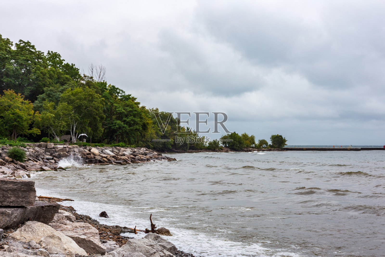 风景如画的湖岸，郁郁葱葱的树木，岩石海岸线和多云的天空照片摄影图片