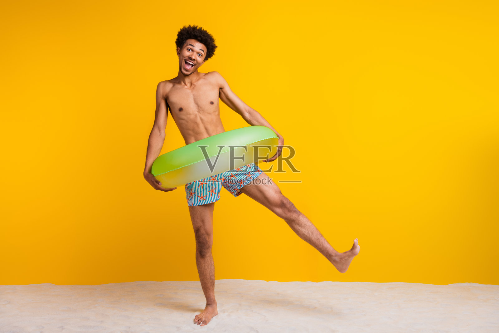 阳光明媚的光头年轻男子，留着非洲卷发，手持充气圈，背景为鲜艳的黄色。照片摄影图片