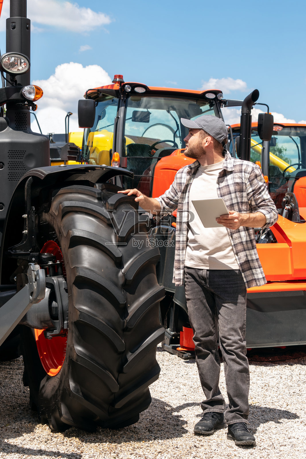 在经销商处，站在户外的男子手持数字平板，旁边是建筑和农业机械。照片摄影图片