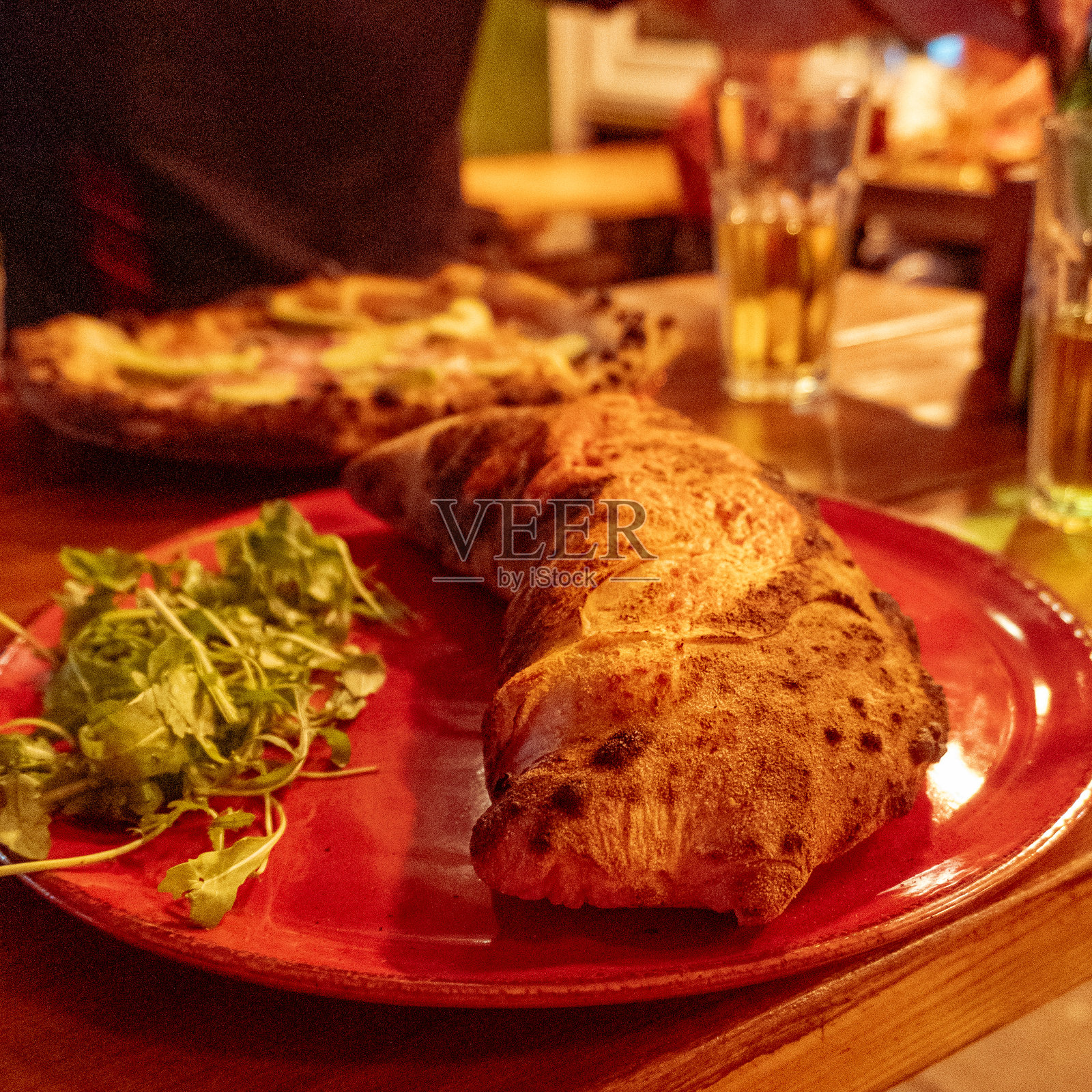 红盘子上的披萨卡尔佐内，放在木桌上。用传统披萨烤箱烘烤的那不勒斯披萨。意大利食谱晚餐。英国巴斯。照片摄影图片