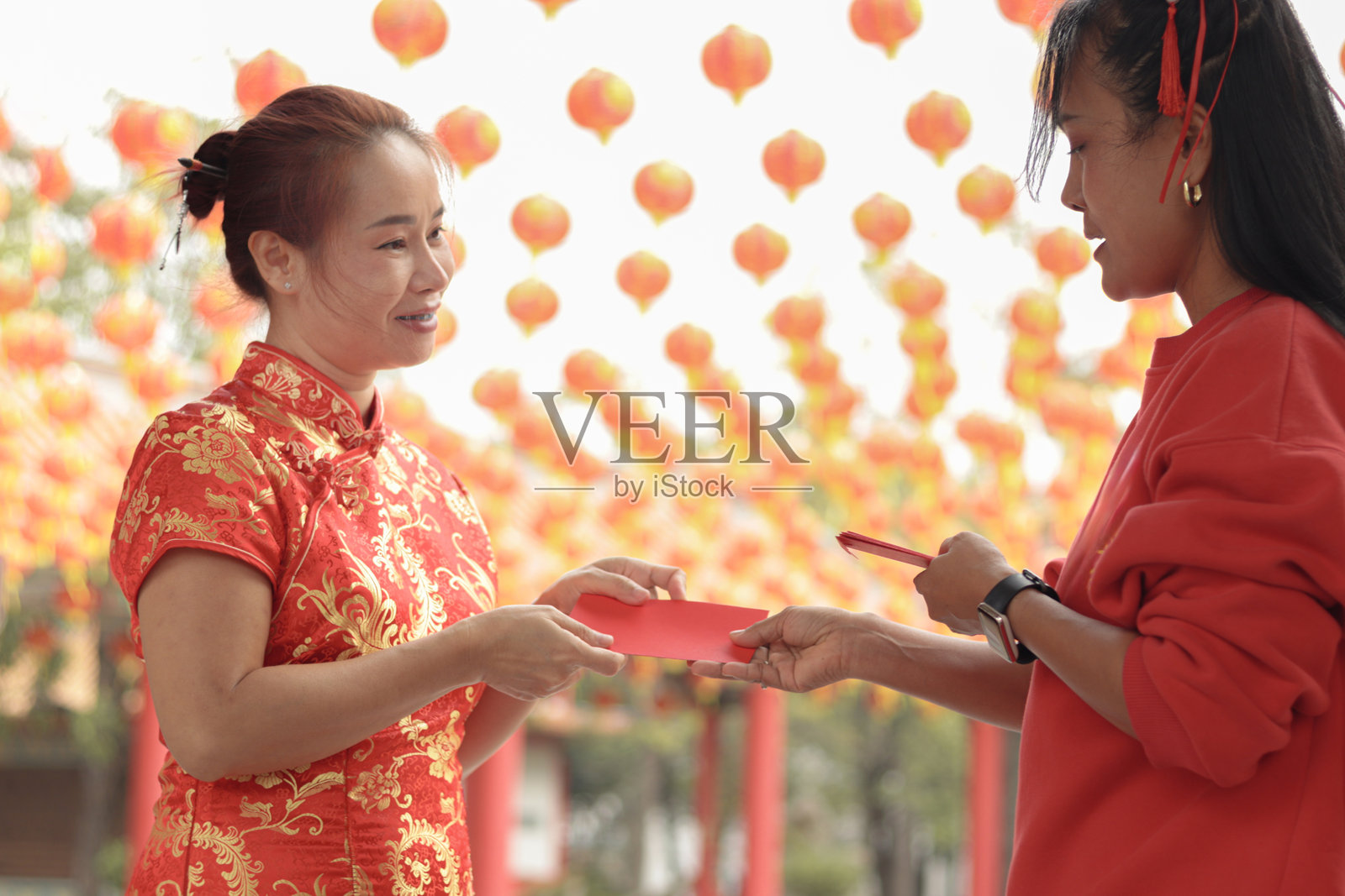 穿着传统红色旗袍的亚洲女性在中国建筑中接受家人赠送的红包。人们与家人和朋友一起庆祝春节。照片摄影图片