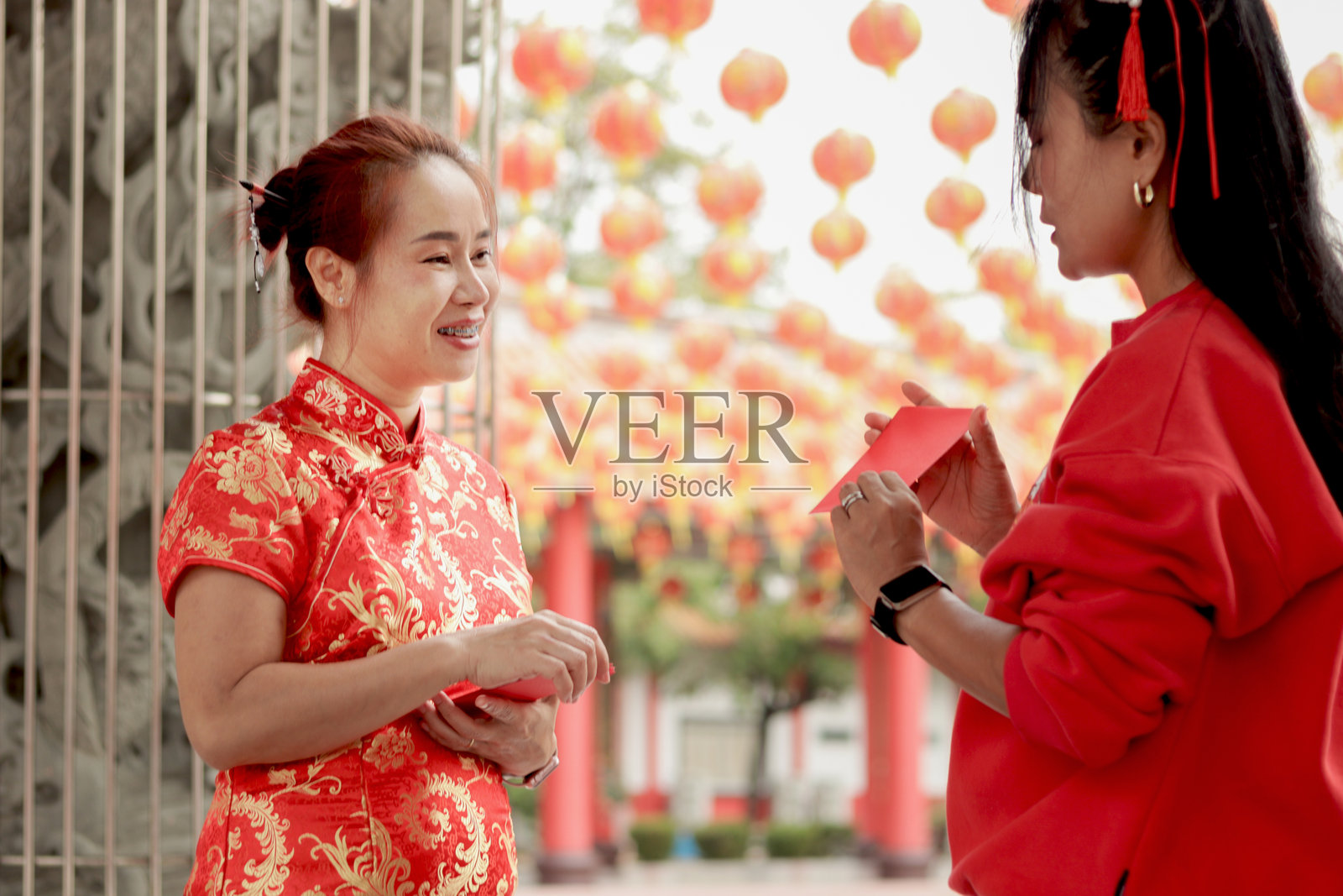 穿着传统红色旗袍的亚洲女性在中国建筑中接受家人赠送的红包。人们与家人和朋友一起庆祝春节。照片摄影图片