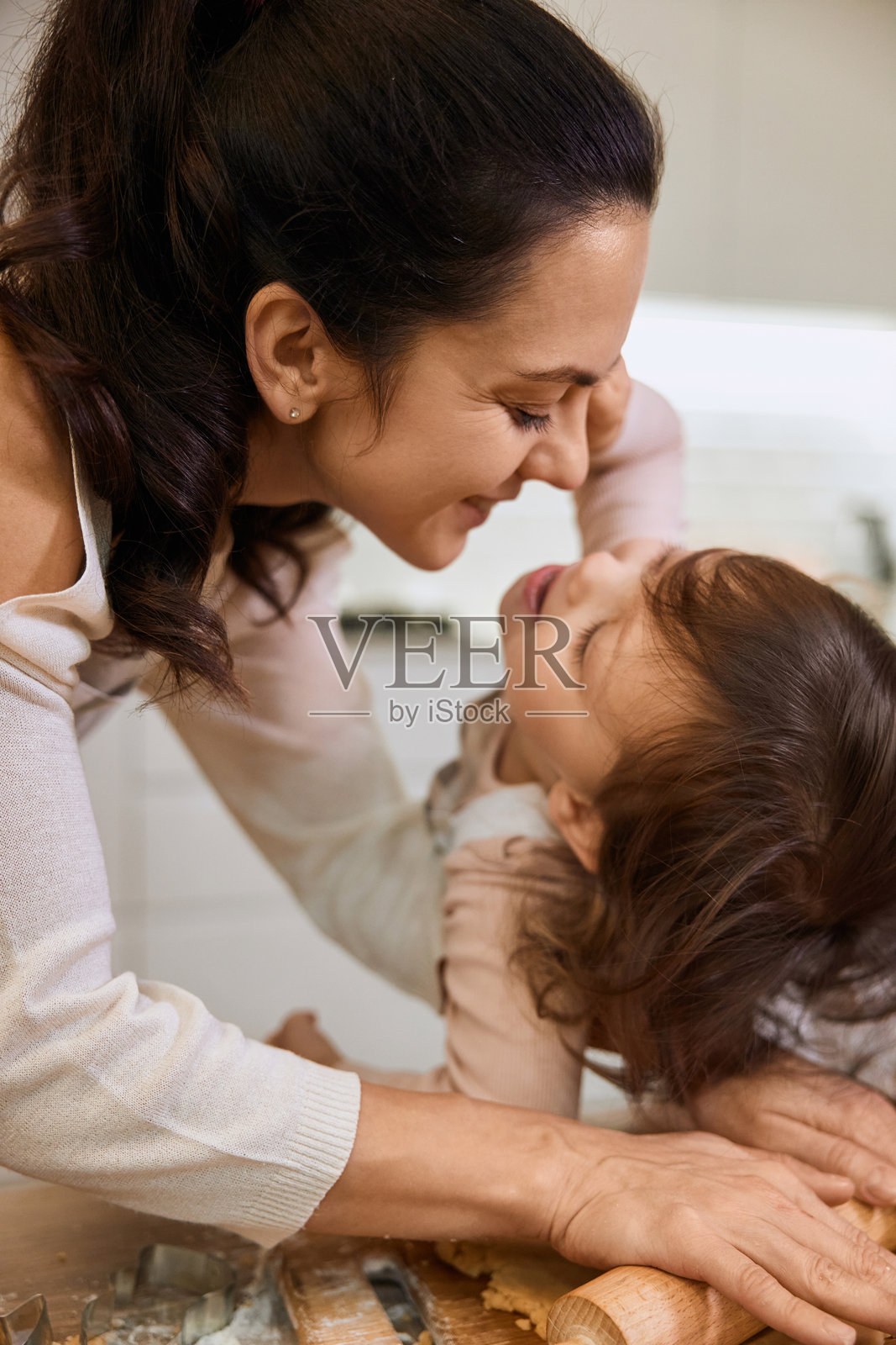 母亲和小女儿一起擀制自制糕点的面团。照片摄影图片