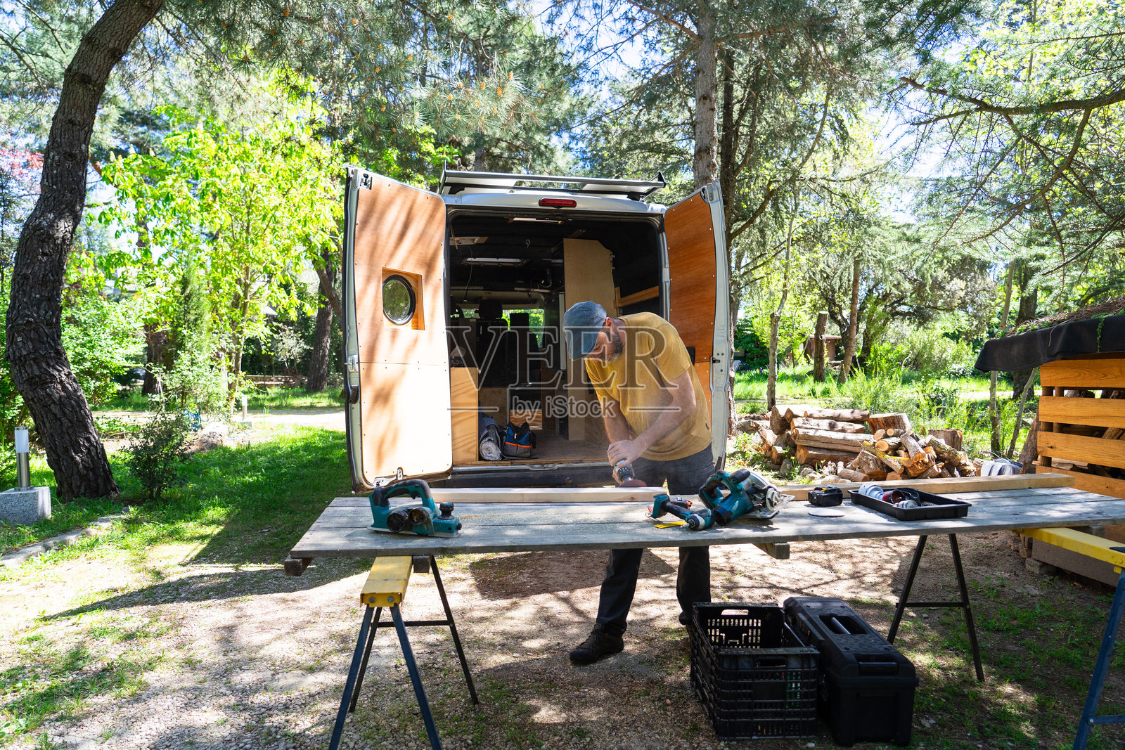 木匠在森林中露营车旁使用电动砂光机打磨木板照片摄影图片