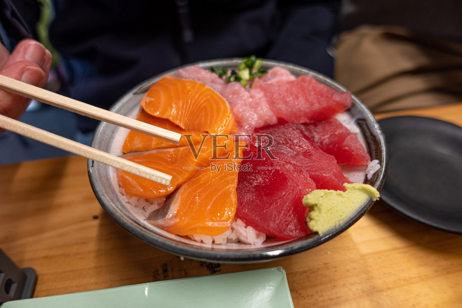 一个人正在用筷子享用一碗寿司。三文鱼。芥末。金枪鱼。米饭。照片摄影图片