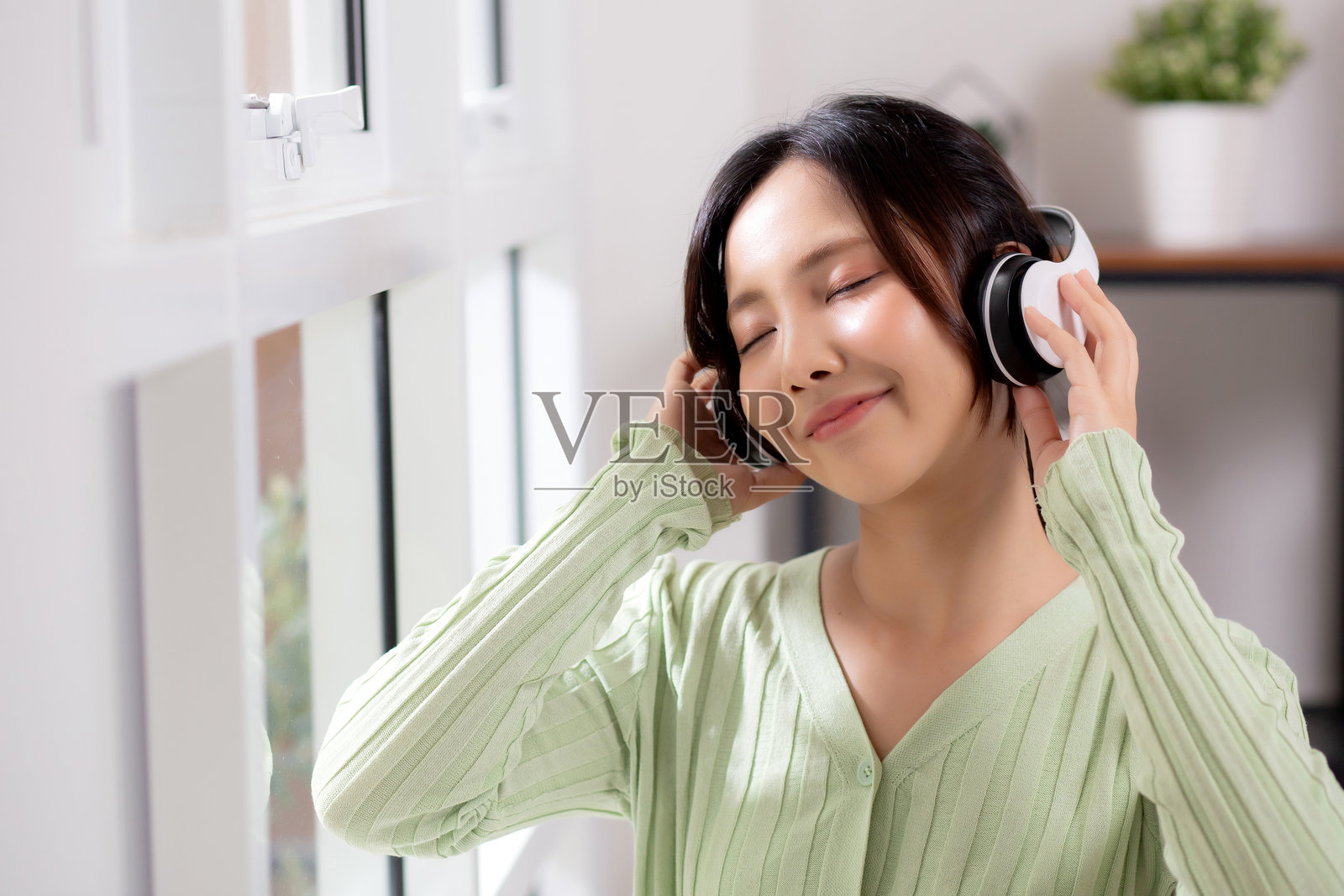 快乐的年轻女性戴着耳机在家中的客厅里享受音乐，充满乐趣和快乐，体现了女性的幸福与娱乐，生活方式概念。照片摄影图片