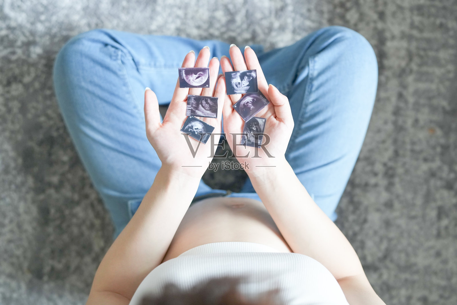 一位20多岁的日本孕妇，穿着显露肚子的裙子，坐在公寓的地毯上，手掌中握着一张小小的超声波照片，凝视着它。照片摄影图片