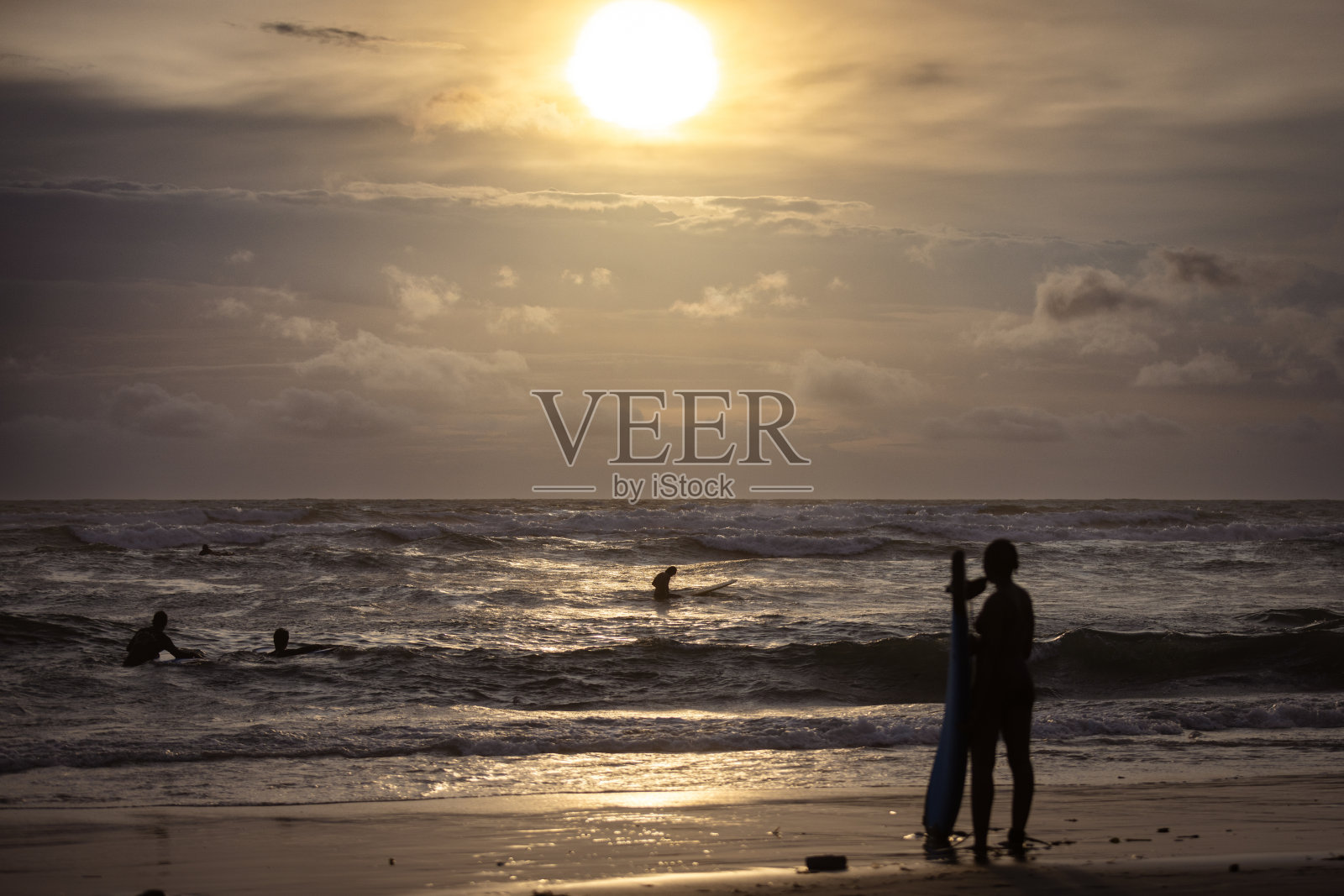 一个无法辨认的女性在日落时分的沙滩上站着，刚刚冲浪归来。照片摄影图片