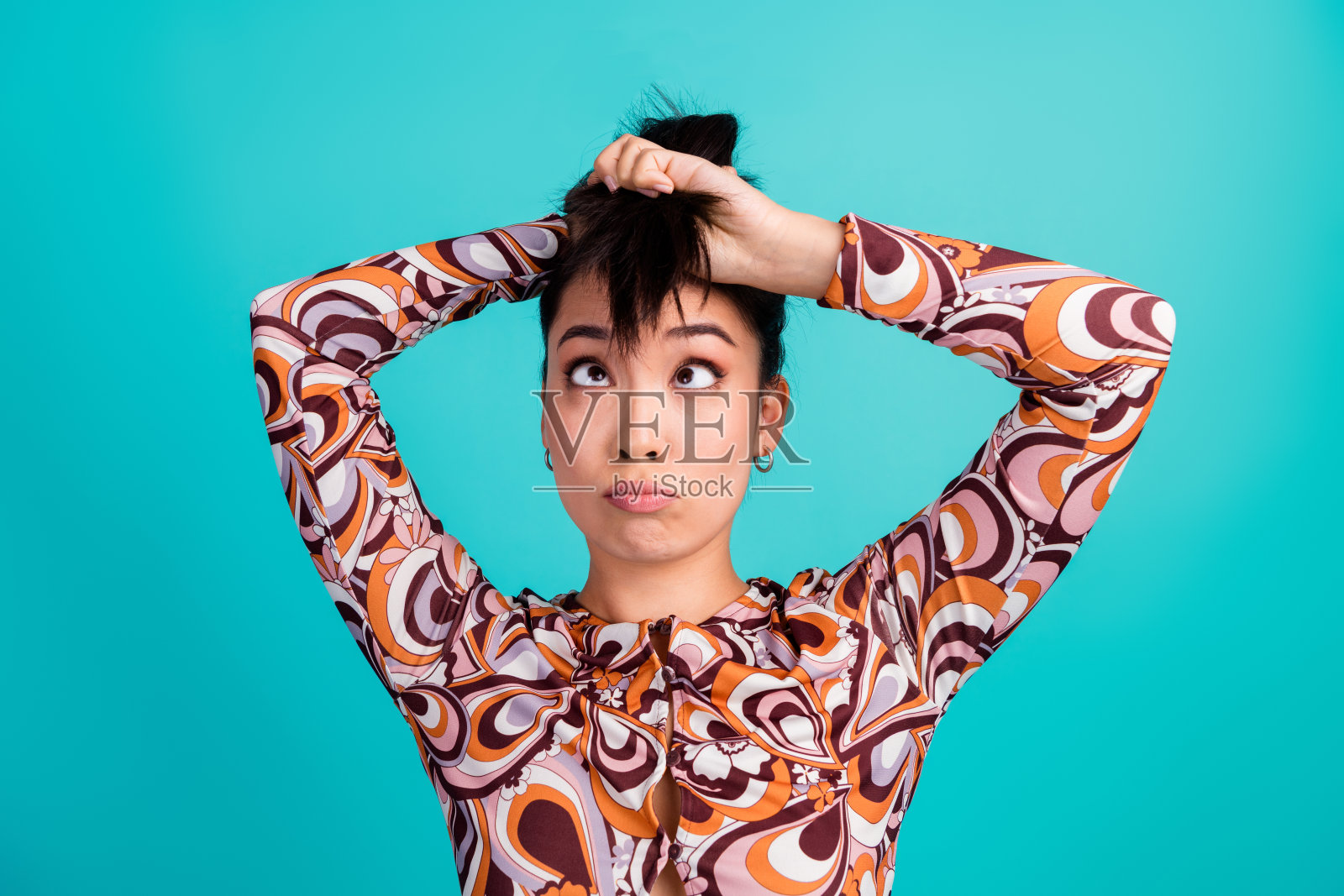 漂亮年轻女孩的照片肖像，表情困惑而惊讶，头发时尚，穿着色彩缤纷的衣服，背景为青色。照片摄影图片