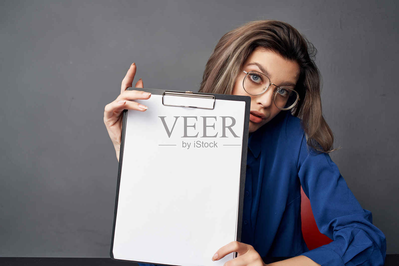 戴眼镜的女商人在桌子旁坐着，手中拿着空白空间。照片摄影图片