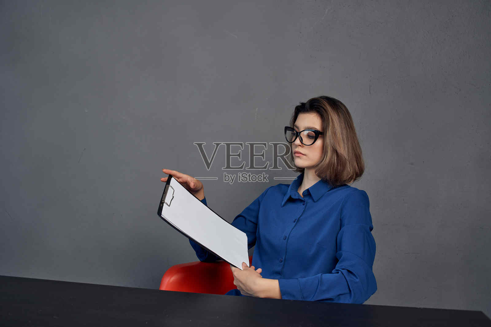 一位穿着蓝色衬衫的女性坐在桌旁，手中拿着一个文件夹和一些文件。照片摄影图片