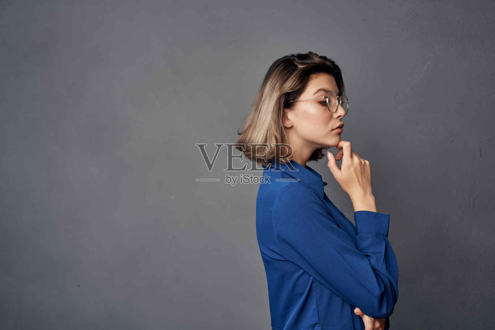 穿着蓝色衬衫、戴着眼镜的优雅女性，背景为单色。照片摄影图片