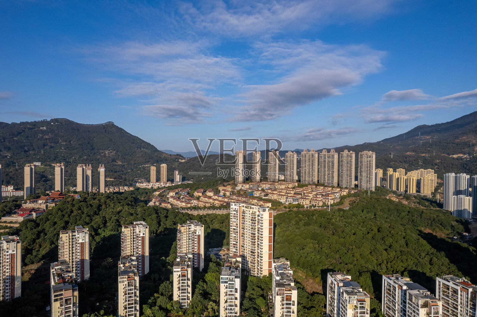 阳光明媚的日子，城市高层住宅楼和别墅在绿树之间的鸟瞰图照片摄影图片