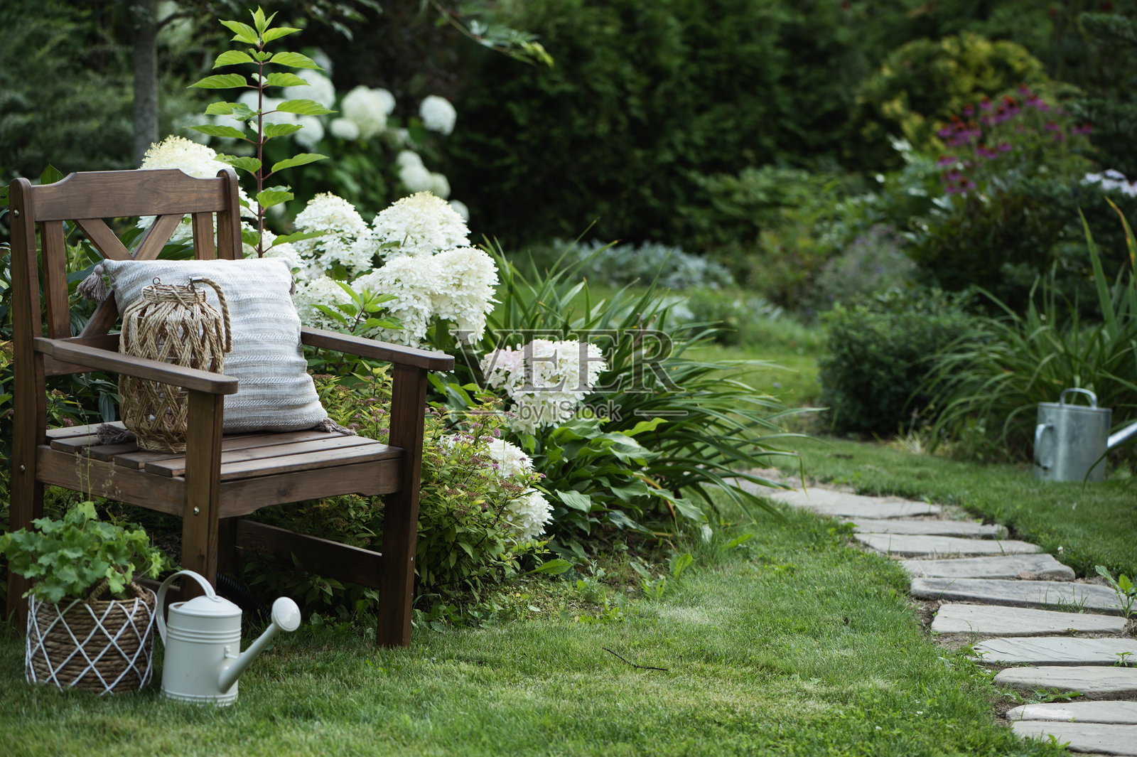 夏季装饰花园景观，盛开的圆锥绣球花和带有舒适靠垫及装饰的木椅。户外休息。照片摄影图片