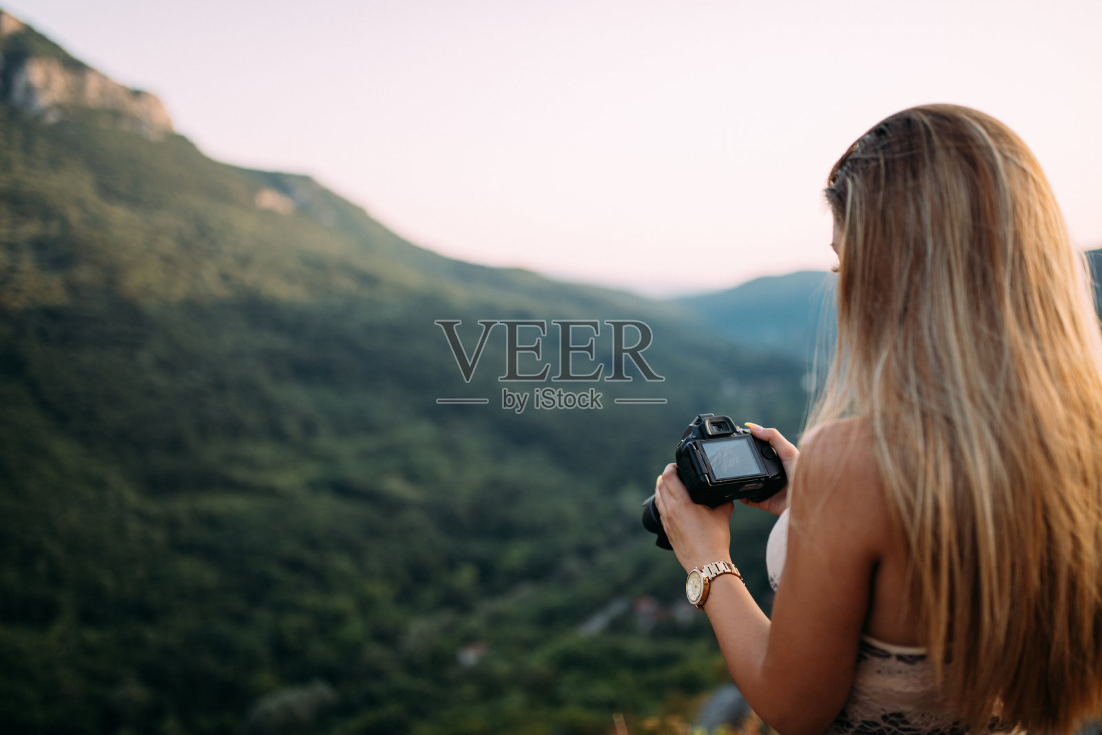 美丽的年轻女性在日落时分的风景如画的山脉中查看相机里的照片照片摄影图片