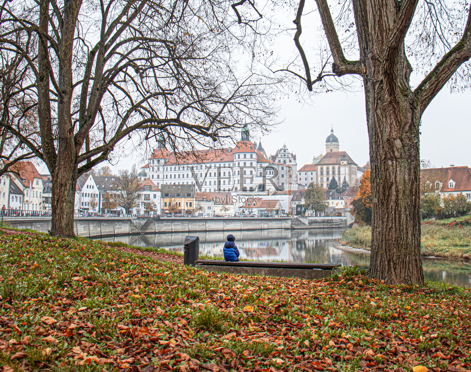 男孩坐在多瑙河边的长椅上，古老的城堡和跨越多瑙河的桥，秋季的堤岸，德国纽堡，2024年10月28日照片摄影图片