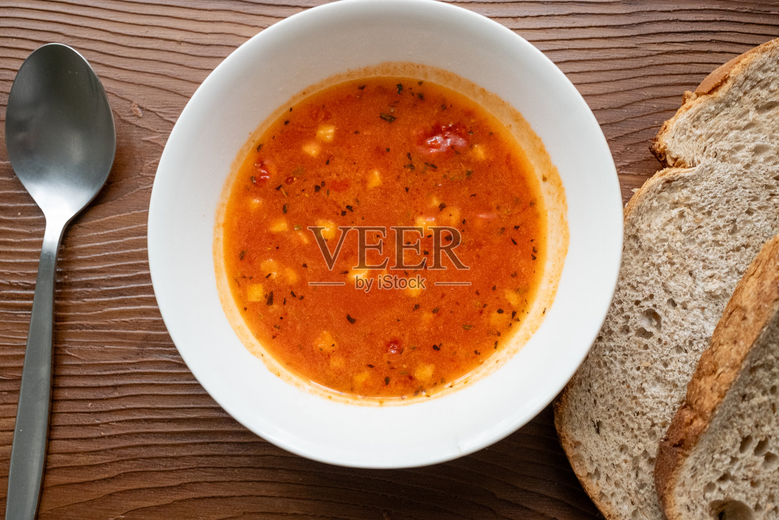 碗里的番茄汤放在木桌上，旁边有几片面包。照片摄影图片