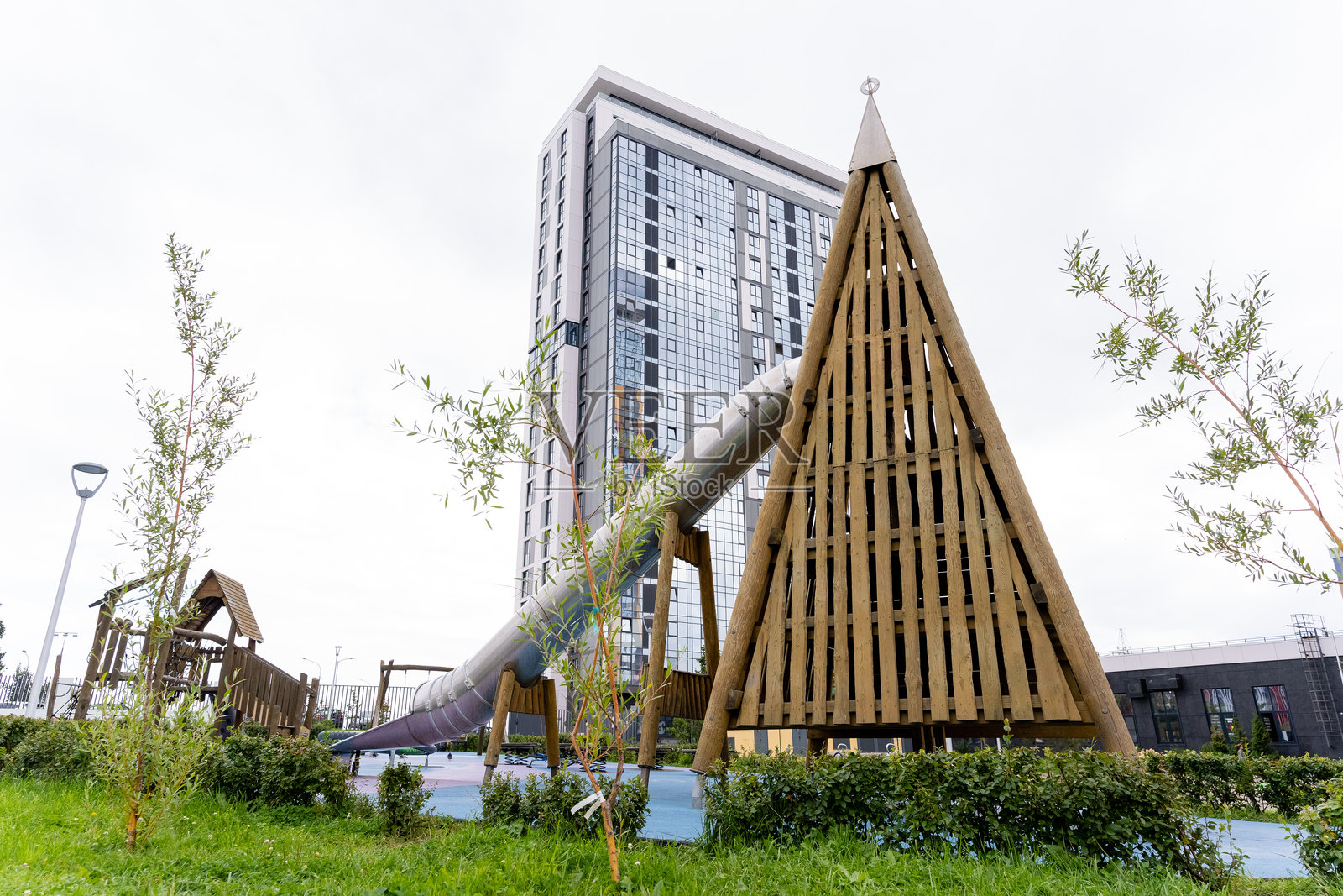 一个有滑梯和三角形结构的游乐场，靠近一栋高楼照片摄影图片