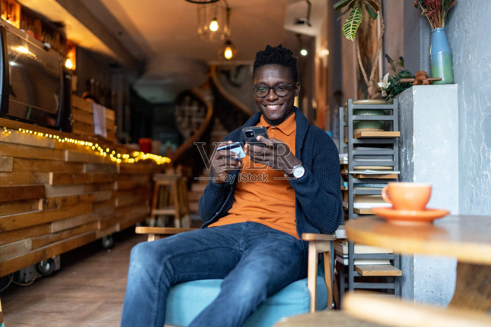 年轻男子坐在咖啡馆里，用手机和信用卡进行在线购物照片摄影图片