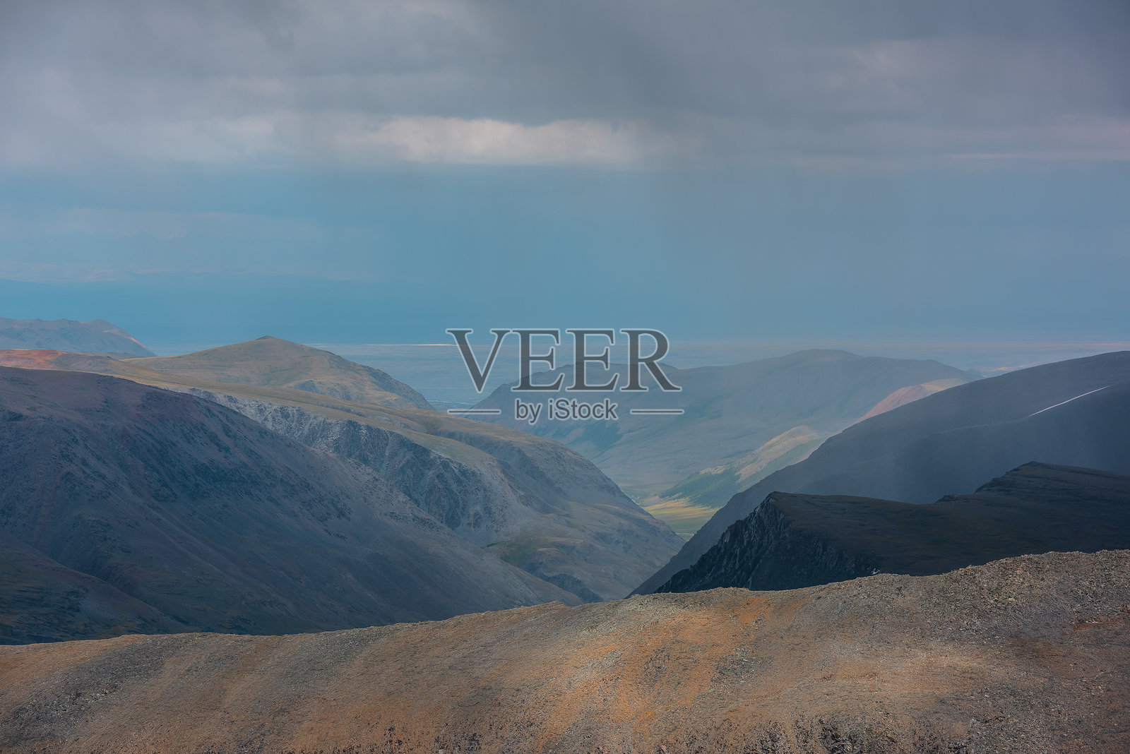 戏剧性的分层鸟瞰图，俯瞰大型尖锐山脊，阳光照耀下的绿色高山深谷，远处的大悬崖在雨中，灰色多云的天空。山脉轮廓在低矮的雨云中隐现。照片摄影图片