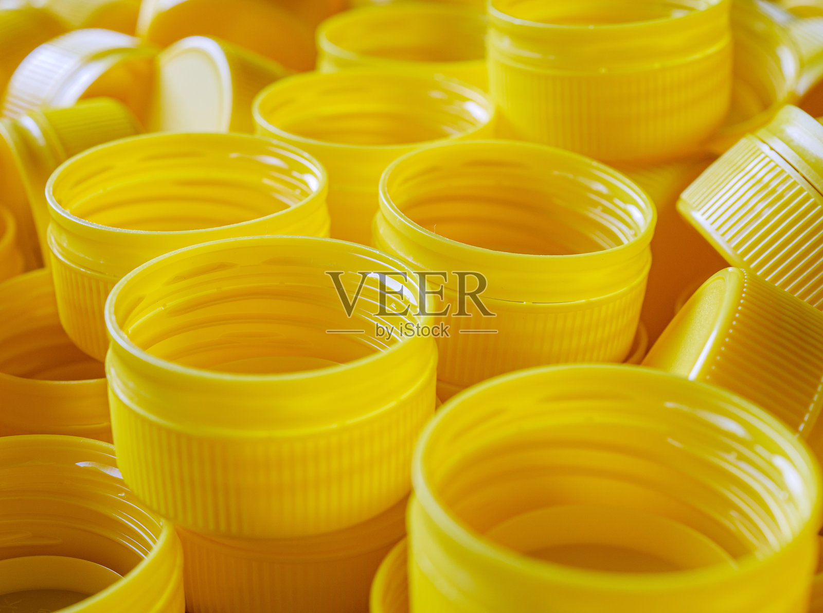 黄色塑料瓶盖。回收收集和生产加工塑料瓶盖的背景，工业生产的高密度聚乙烯黄色瓶盖特写。照片摄影图片